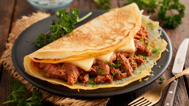 Panqueca de carne à la française servida em uma mesa rústica, com queijo derretido e salsa picada.